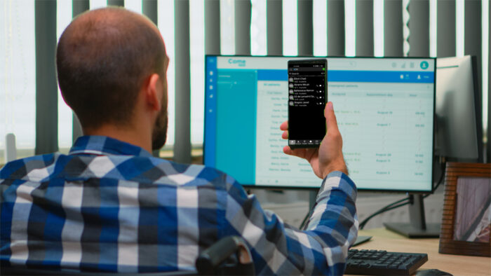 Man holding his smartphone in the air with the 3CX app in front of his computer.